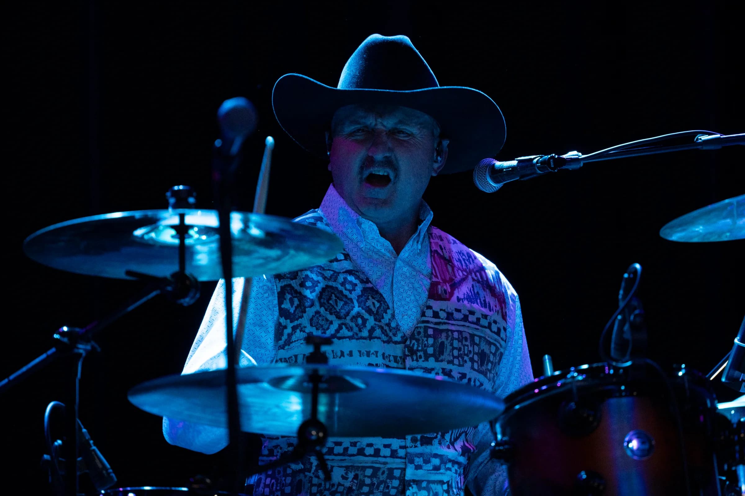 Drummer performing behind the cymbals under blue lighting