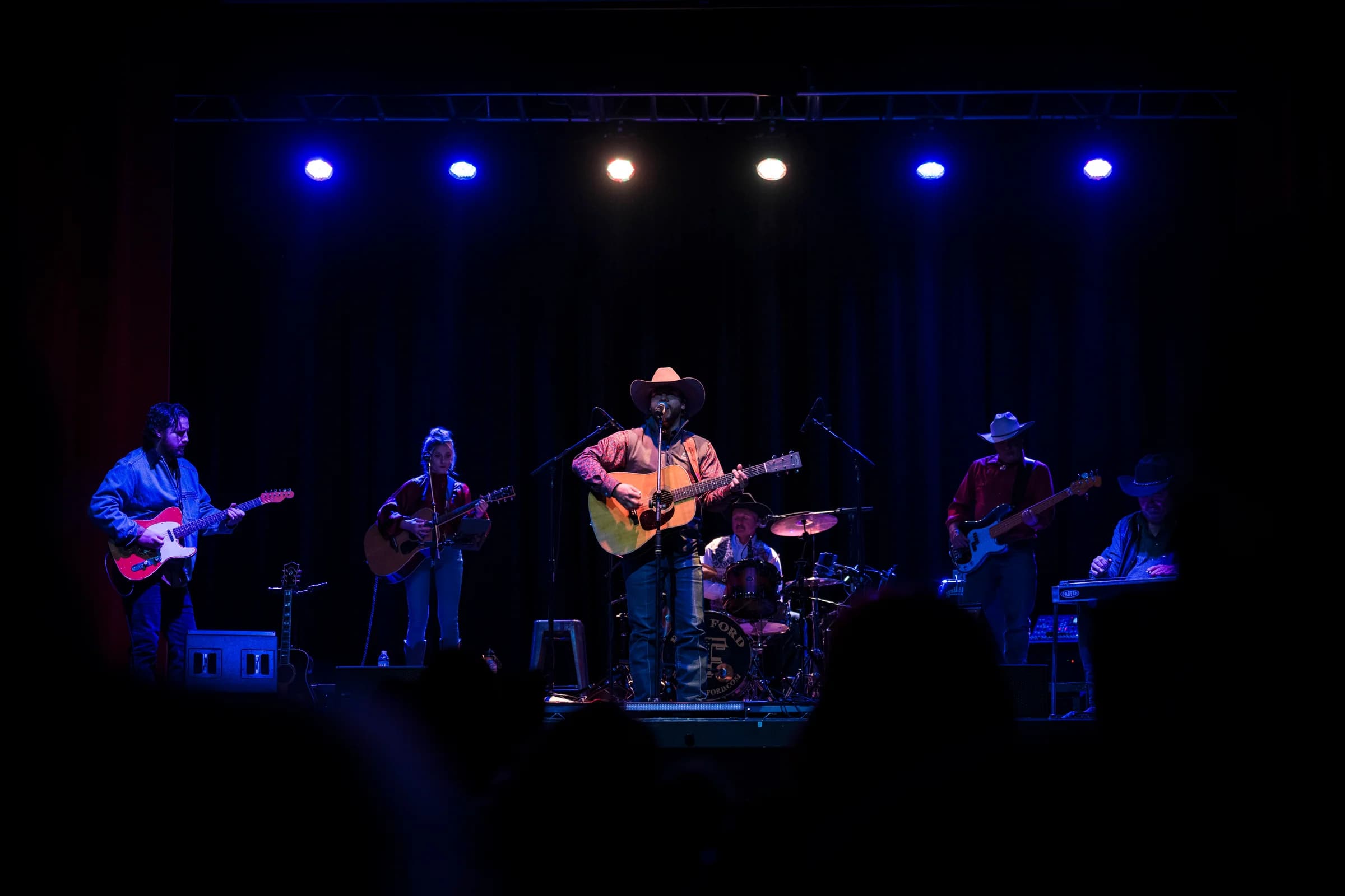 Buck Ford and the band on a dark stage with blue overhead lights