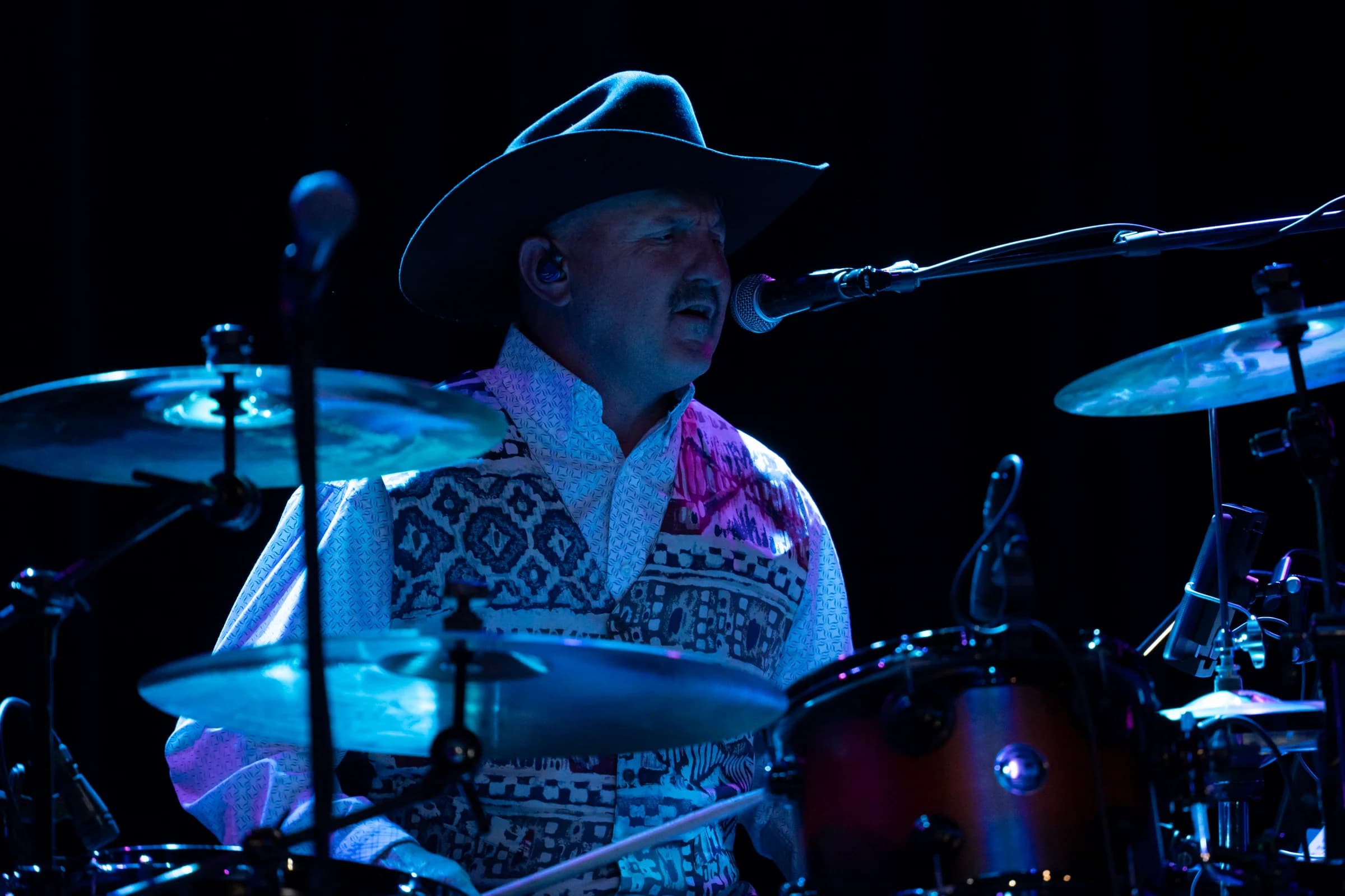 Drummer in a cowboy hat behind the kit under blue lights