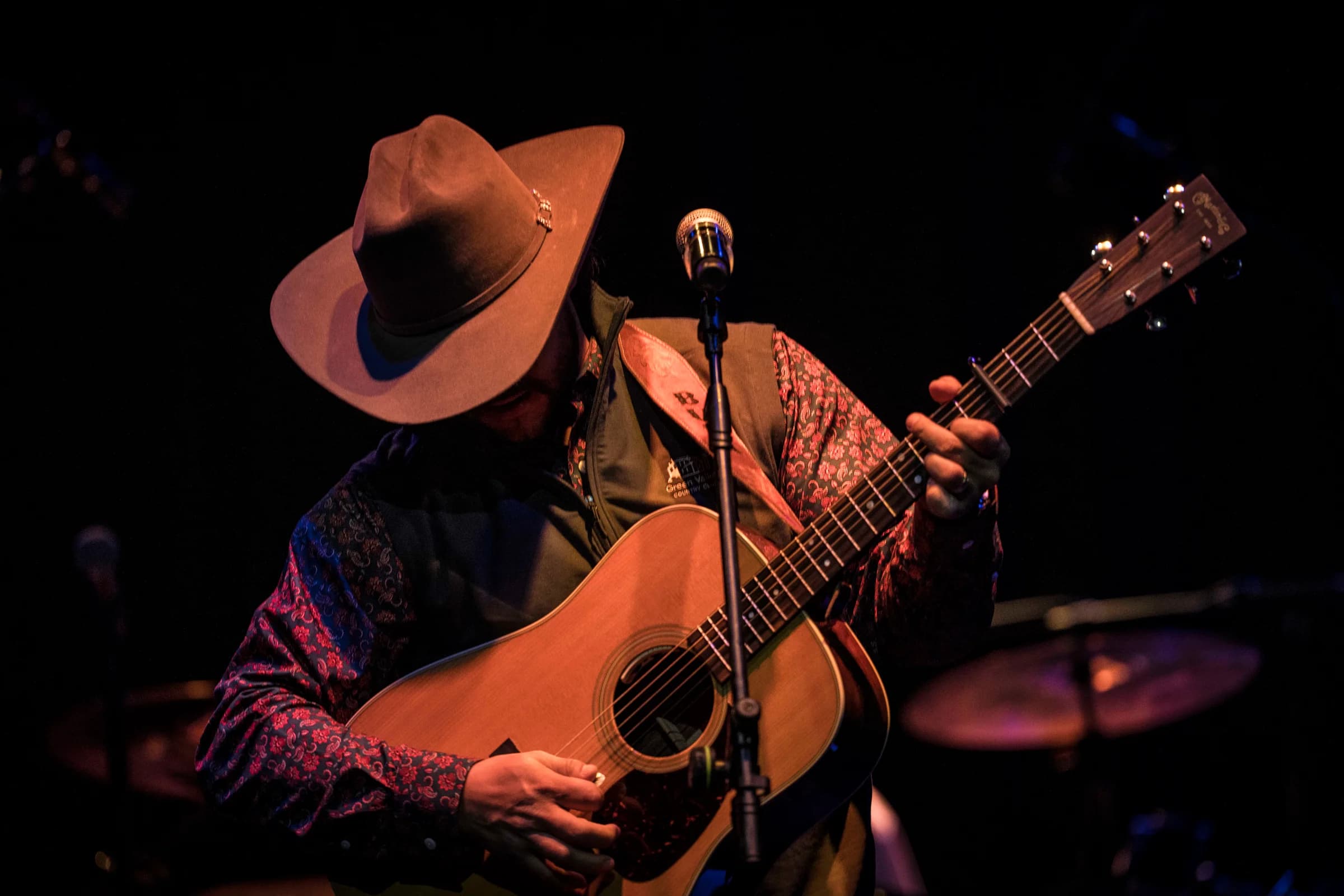 Buck Ford looking down at his acoustic guitar under a warm spotlight