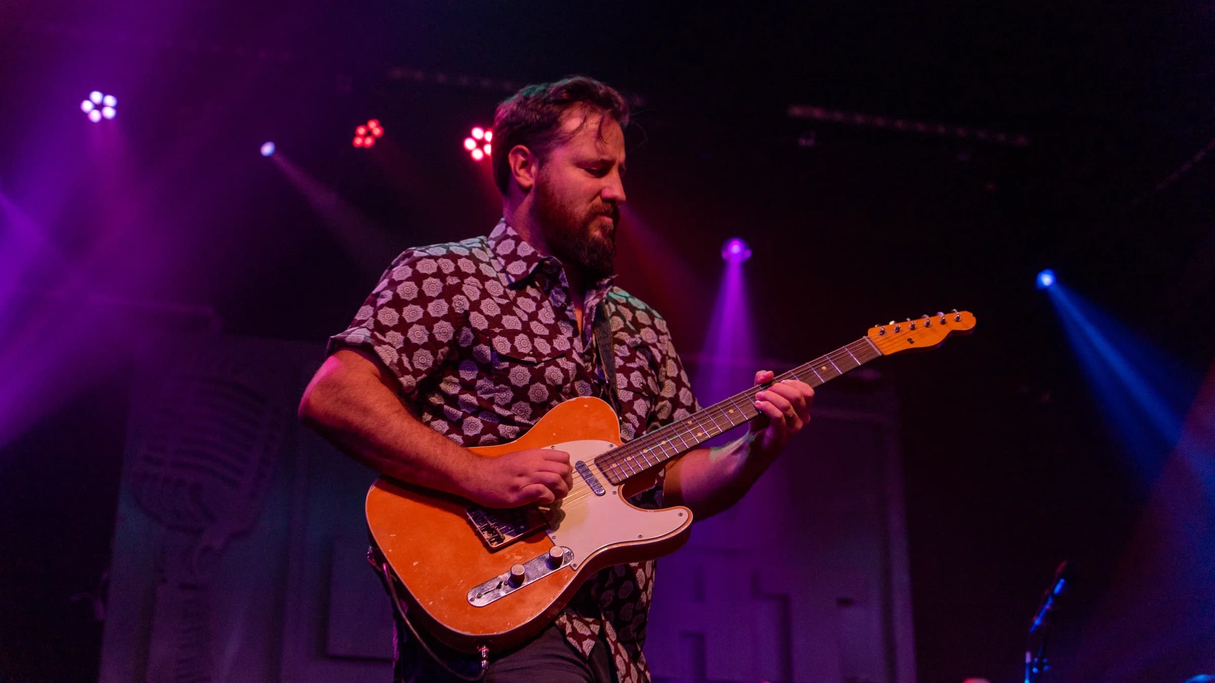 Electric guitarist playing a solo under purple lighting