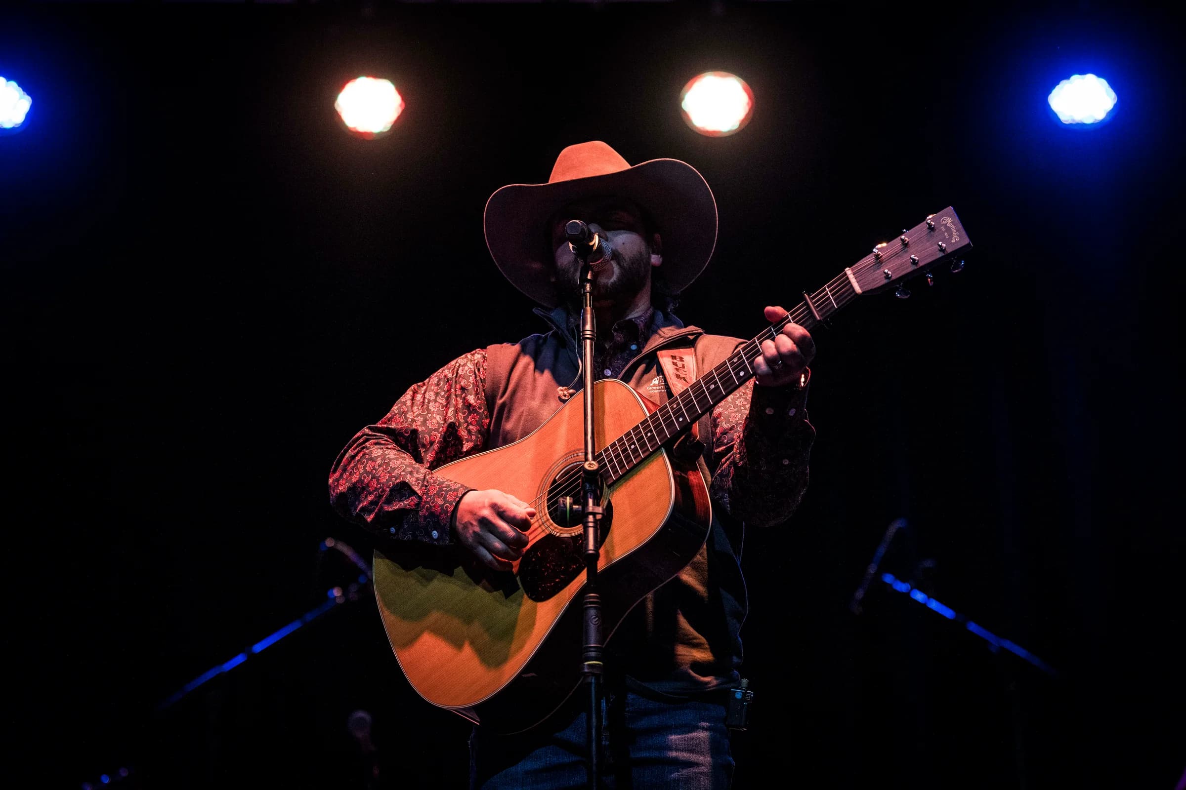 Buck Ford singing and playing guitar under red lighting