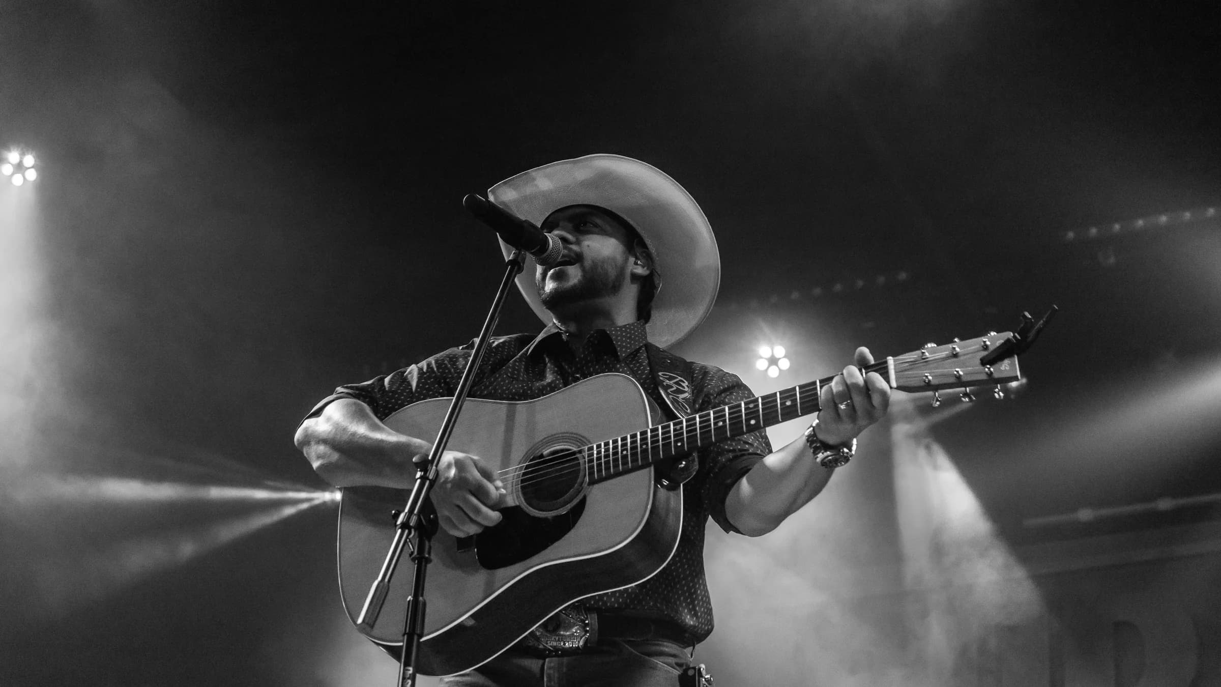 Buck Ford playing acoustic guitar under a stage spotlight