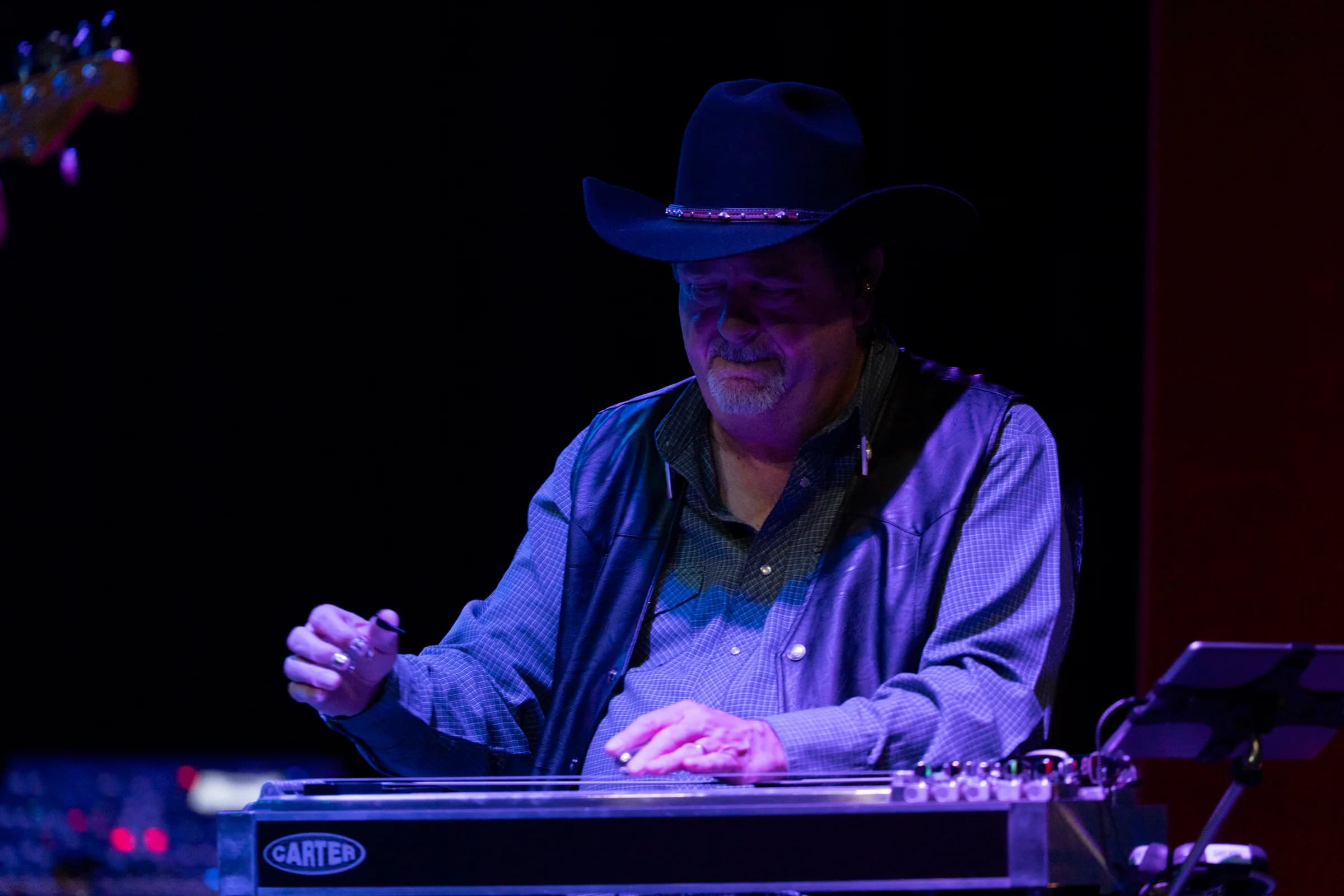 Steel guitarist seated at his instrument under purple stage lighting
